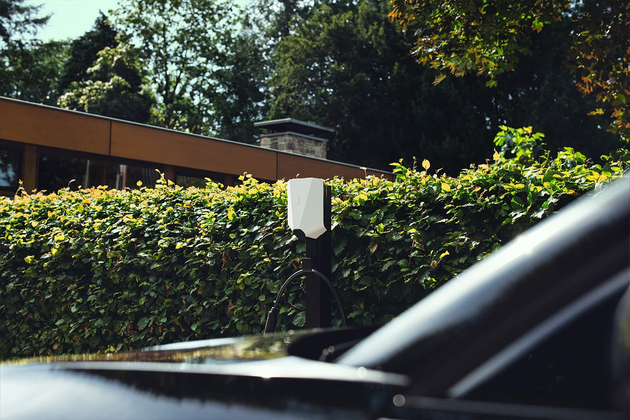 Laadpaal aan een gevel met een elektrische auto op de oprit